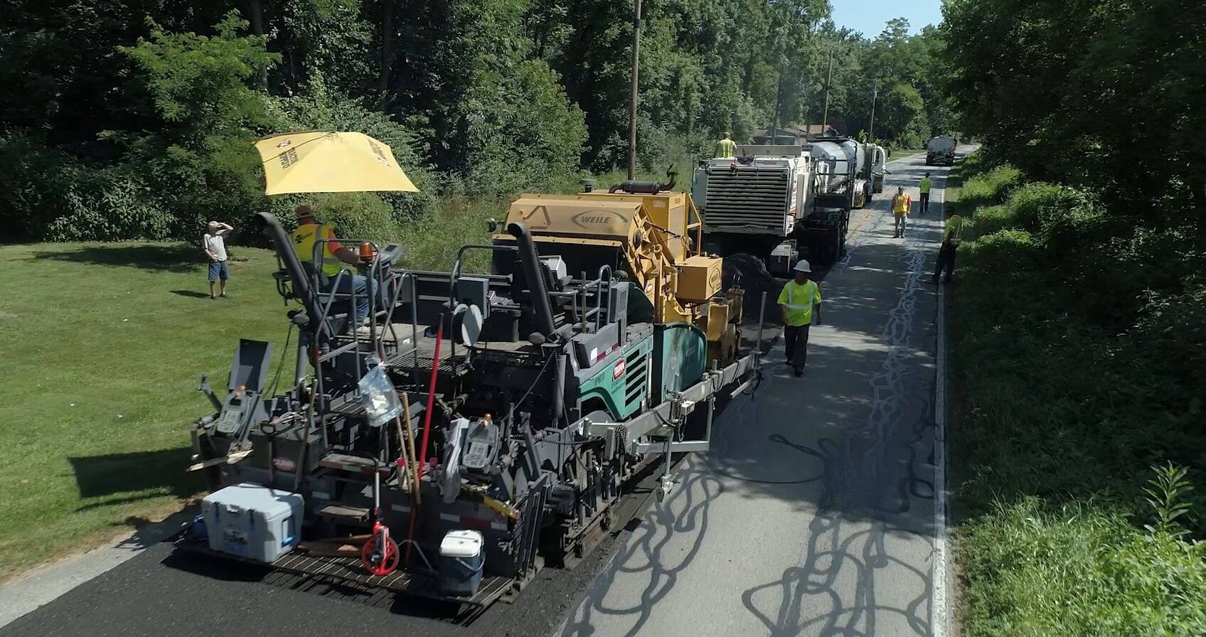 Train of machines line up on a road to perform CIR which mills the top of the pavement, combines it with asphalt emulsion and lays it back down on the road