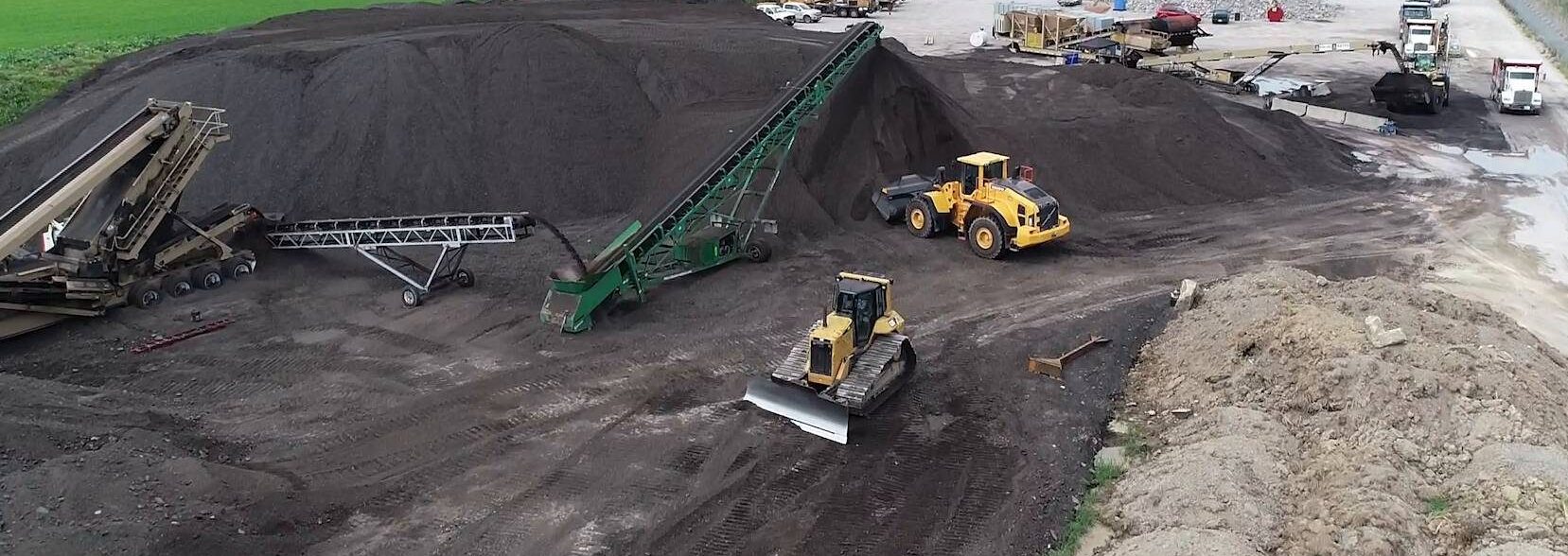 Overhead view of a cold central plant recycling operation. Trucks carry milled asphalt to a recycling machine