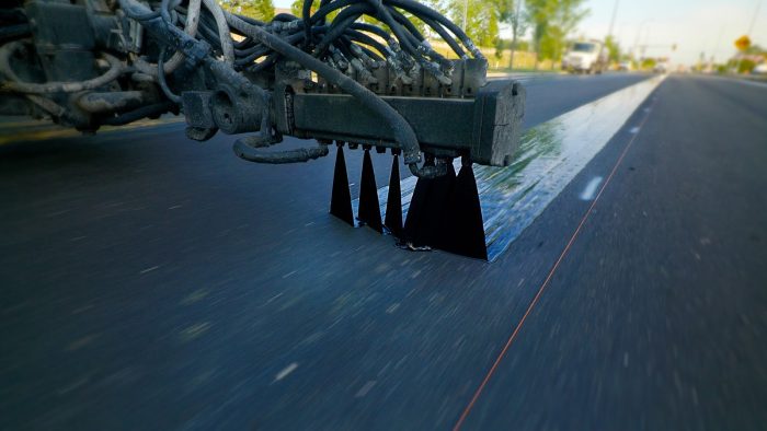 Paving truck dispenses J-Band, a void reducing asphalt membrane, on a road in an 18" wide band of specialized asphalt emulsion. This pavement preservation technique is shiny and sleek