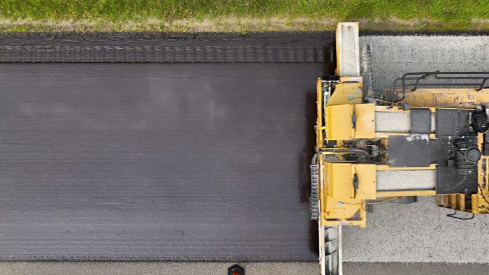 Paving truck dispenses fine aggregate onto a layer of freshly laid asphalt emulsion. 