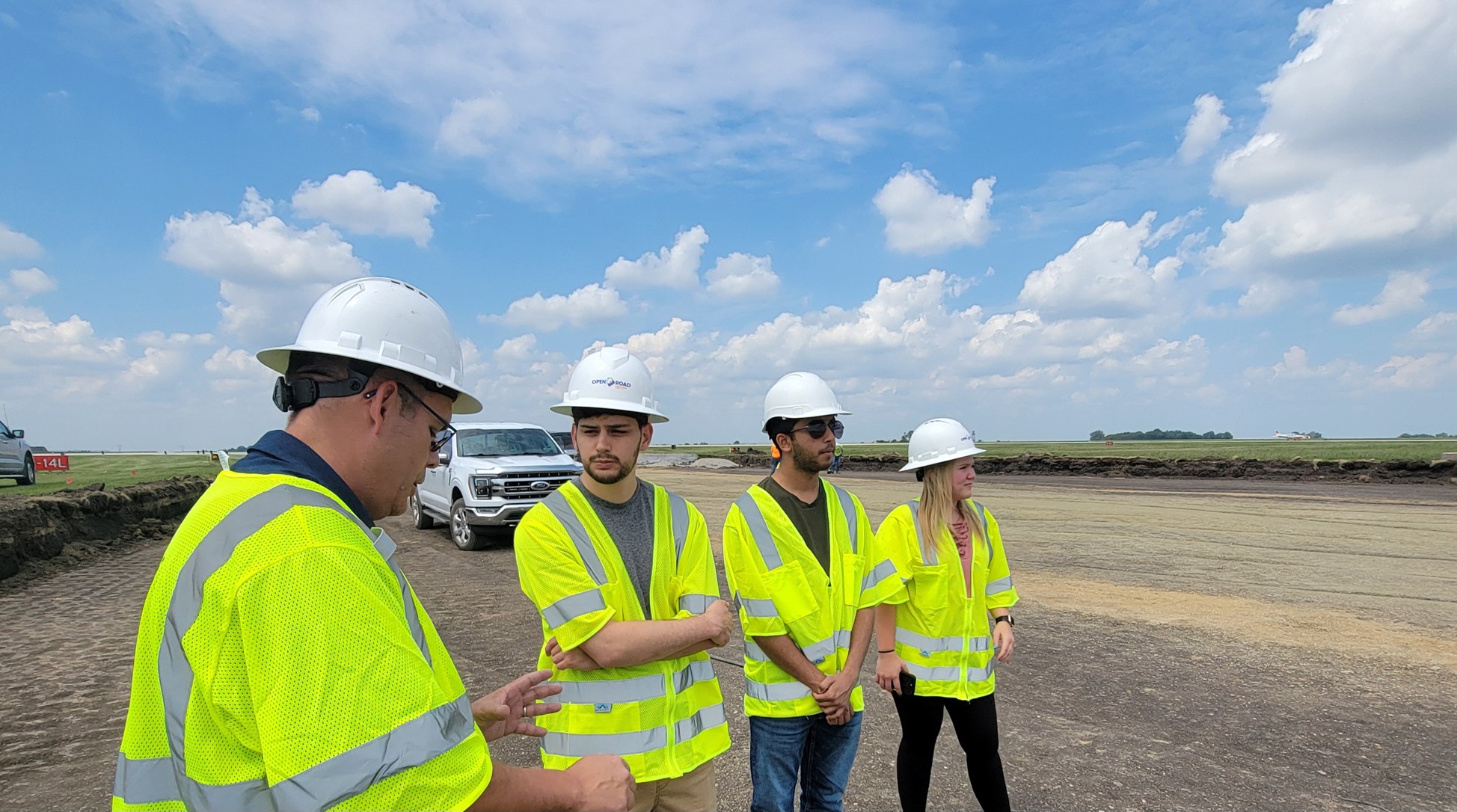 4 people in construction gear stand on an airport job site 