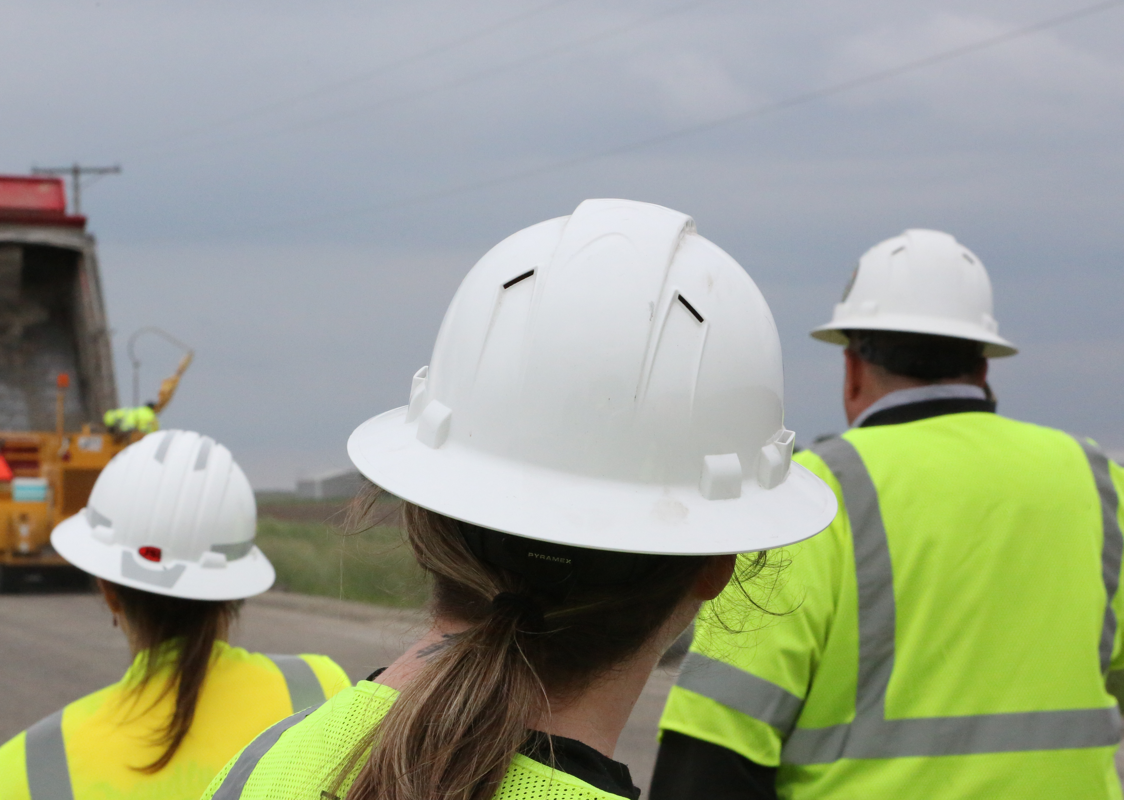 Three paving workers in hard hats and safety gear PPE personal protective equipment